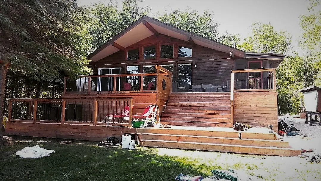 Maison de style cabane avec revêtement en bois traité, terrasse et clôture.