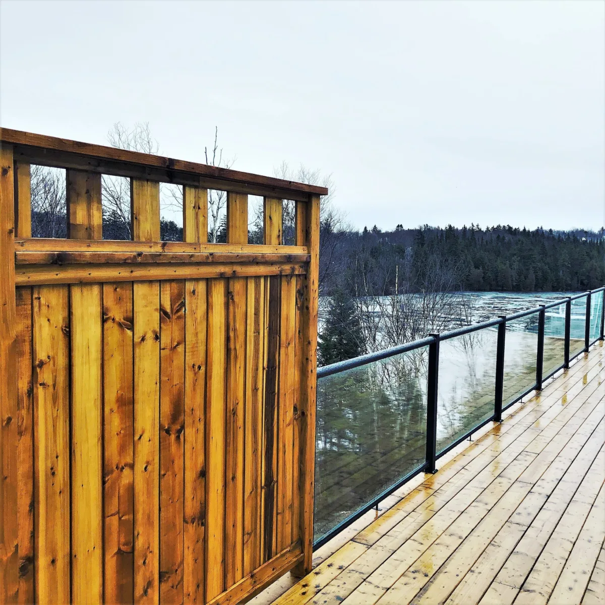 Mur d'intimité en bois sur une terrasse avec une clôture en verre donnant sur le lac.