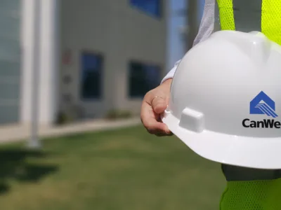 White construction helmet with the Cancel logo in front of a building.