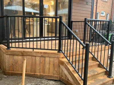 Exterior wooden stairs of a house with black PVC metal railing.