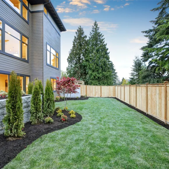 Backyard of a house with professional landscaping and a treated wood fence.